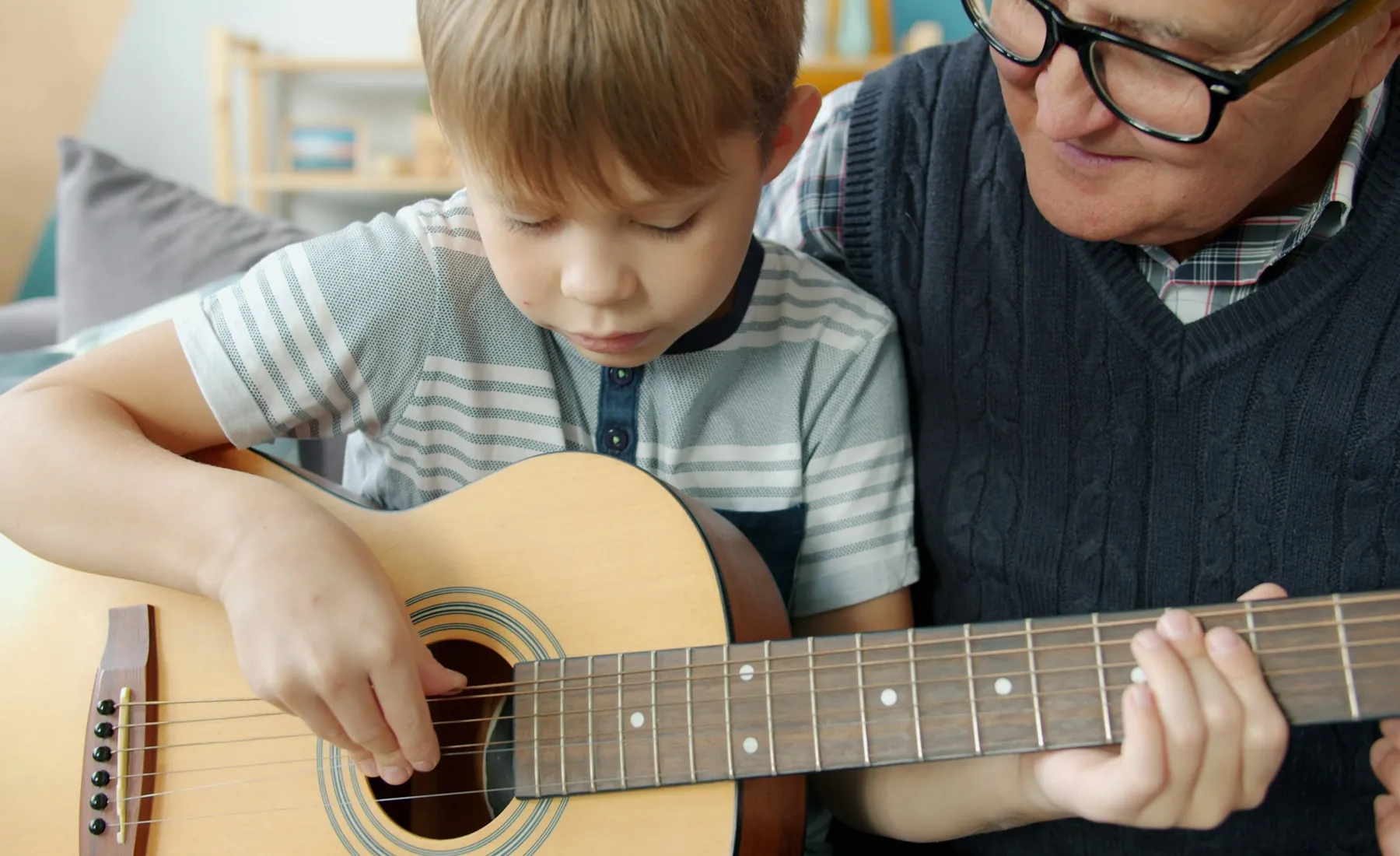 An older man helping a boy place his fingers on a guitar